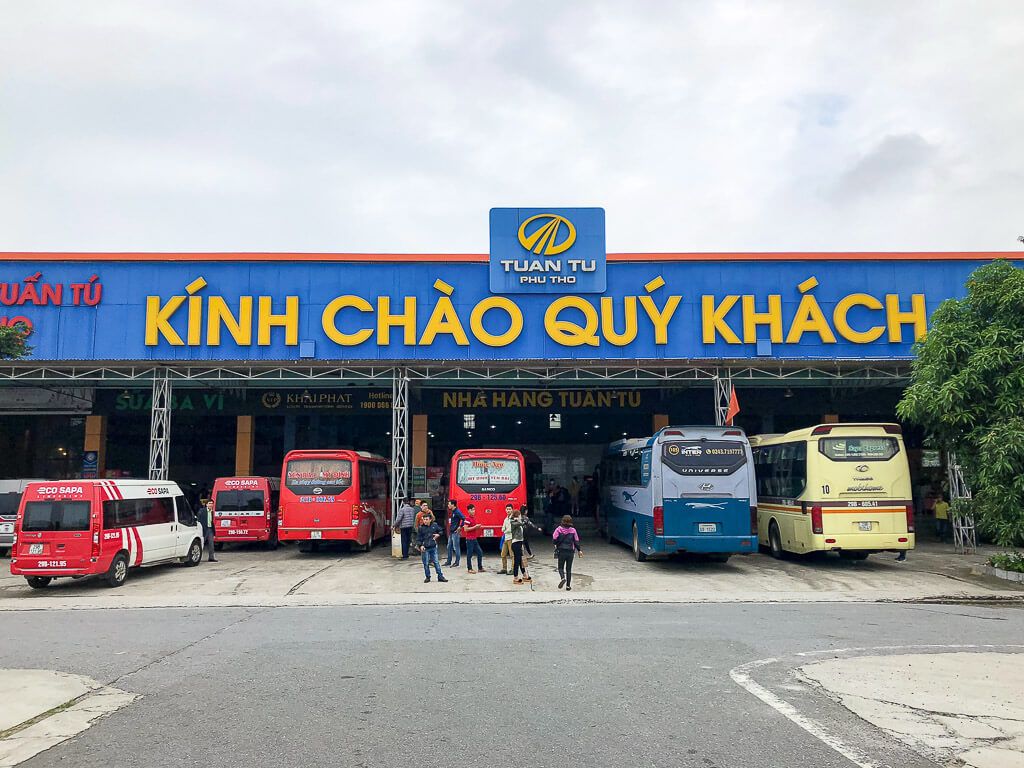 A bus station in Vietnam with customers and several buses