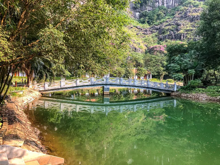 A white wooden bridge crossing over a deep green river at Mua Cave viewpoint or Khu Du Lich Hang Mua Peak