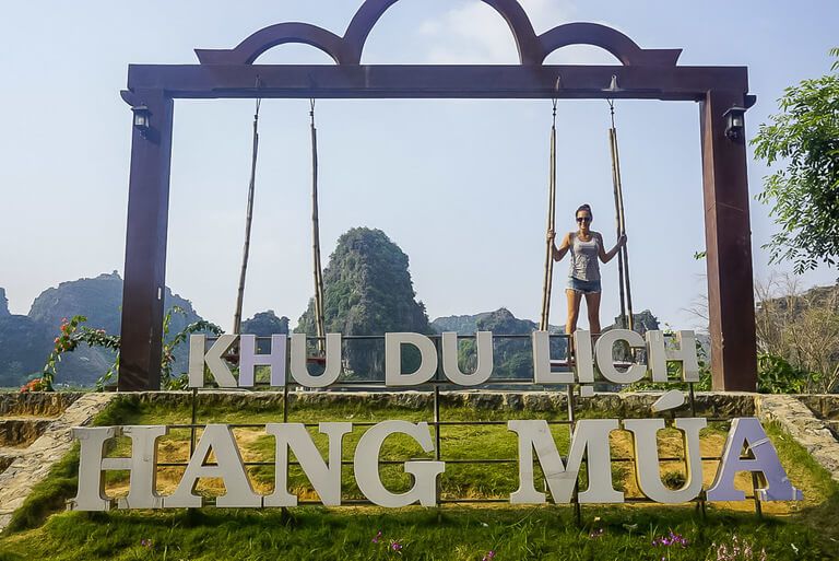 Woman stood on swing in front of the sign for Mua Cave viewpoint or Khu Du Lich Hang Mua Peak
