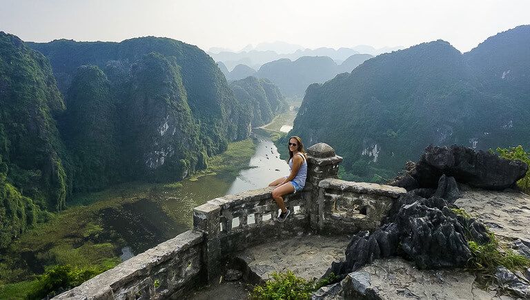 Woman sitting on a stone wall with Tam Coc river in background