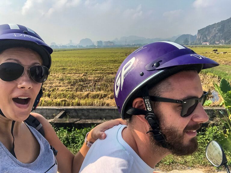 Side shot of man and woman on a motorbike with rice paddies in the background