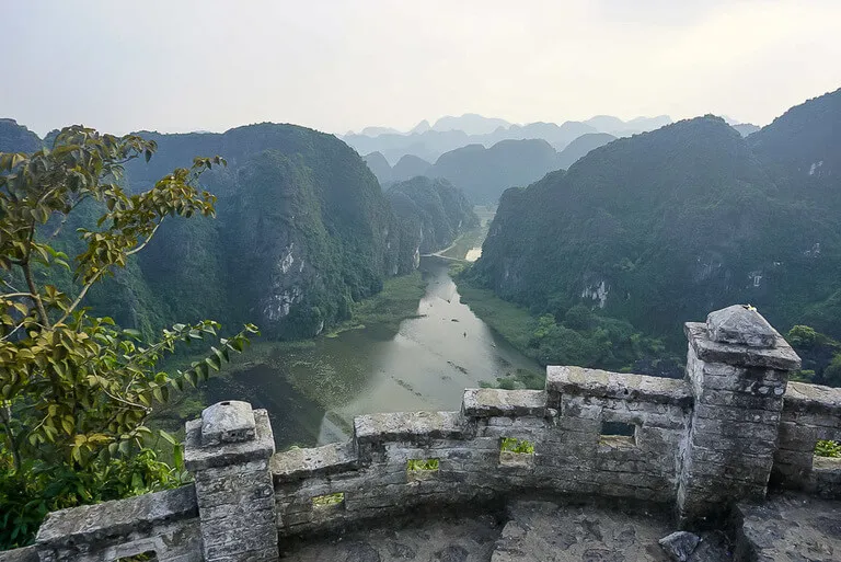 A stone wall in the foreground showcasing a river surrounded by limestone karsts in the background