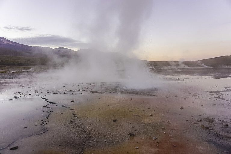 post sunrise geyser field with range of colors on ground near smoke bellowing