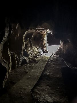 The path leading out of a tiny entrance of the cave with a light at end of tunnel