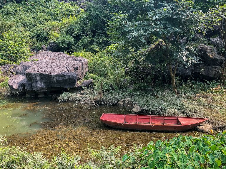 Red boat in a shallow lake surrounded by green vegetation at Bich Dong in Tam Coc