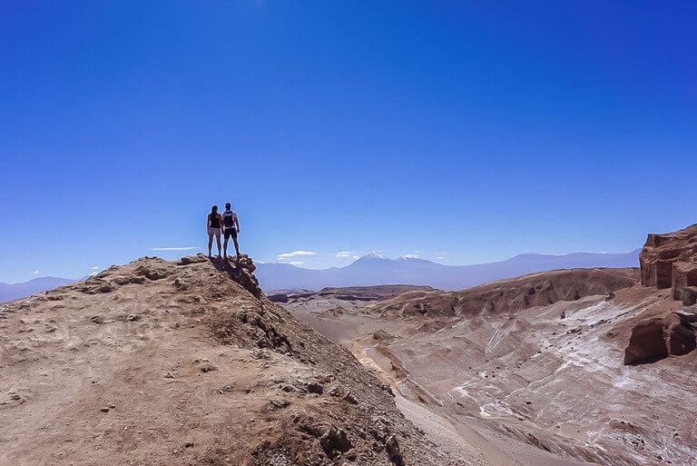 Mark and Kristen stood on edge of rock with amazing view of Valle de la luna and volcano