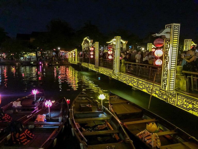 boats on bank of river next to bridge of lights in Hoi An vietnam at night