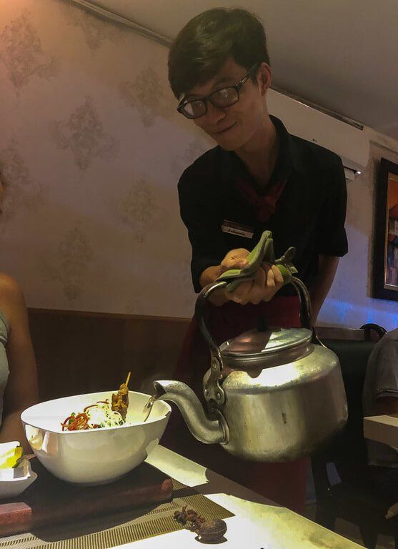 Waiter pouring water into Kristen's broth in Duong's restaurant Hanoi