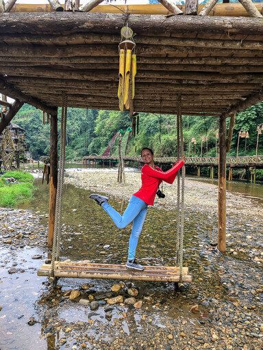 Kristen standing with one leg up on a wooden swing in Cat Cat Village