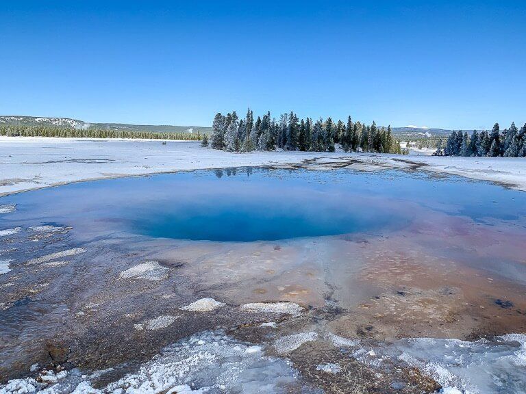 Deep blue hot spring pool surrounded by snow at yellowstone
