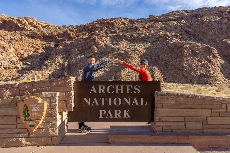 Mark and Kristen Where Are Those Morgans leaning into each other to create an arch above the Arches National Park entrance sign
