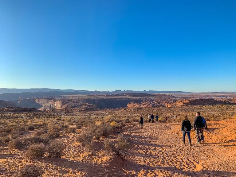 Walking along sandy trail from parking lot to Horseshoe Bend overlook in late afternoon with clear blue sky