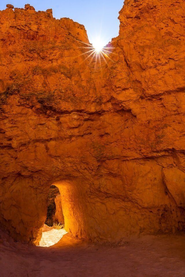 Small arched door carved into huge orange slab of rock and sun starburst at bryce canyon national park utah usa