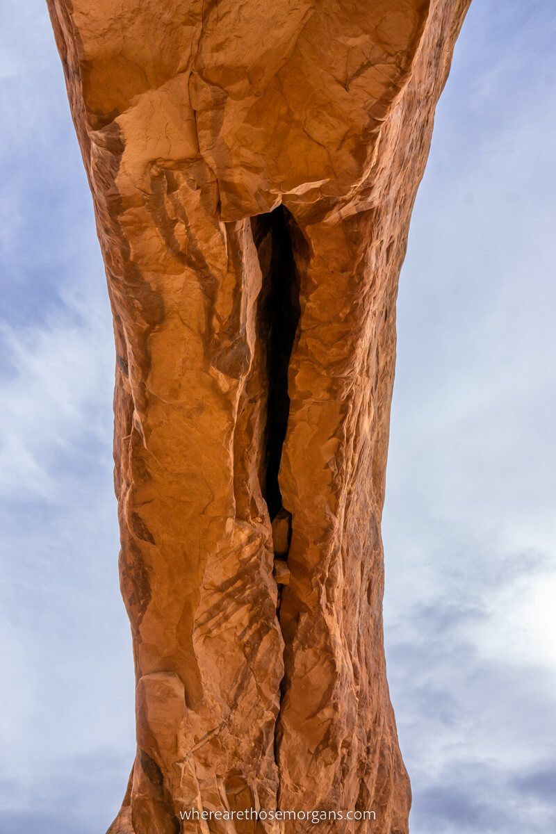 Looking up at a huge sandstone formation with the sky on both sides of the arcing rock