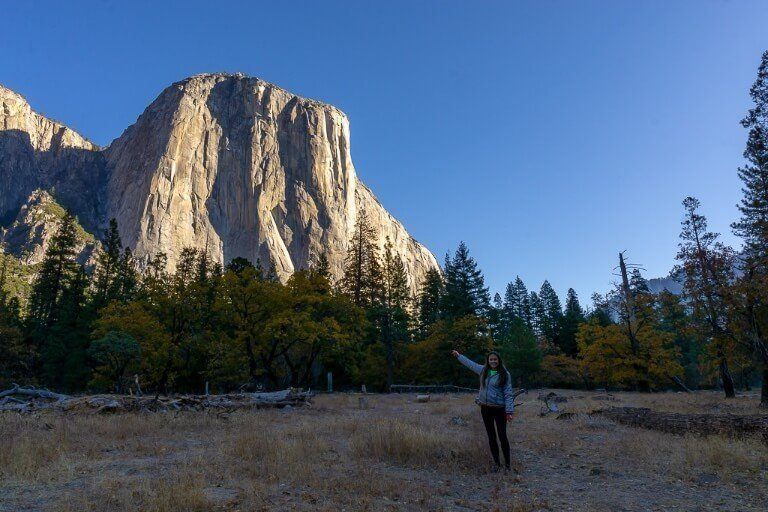 Kristen pointing at El Capitan from a meadow in yosemite national park at sunrise