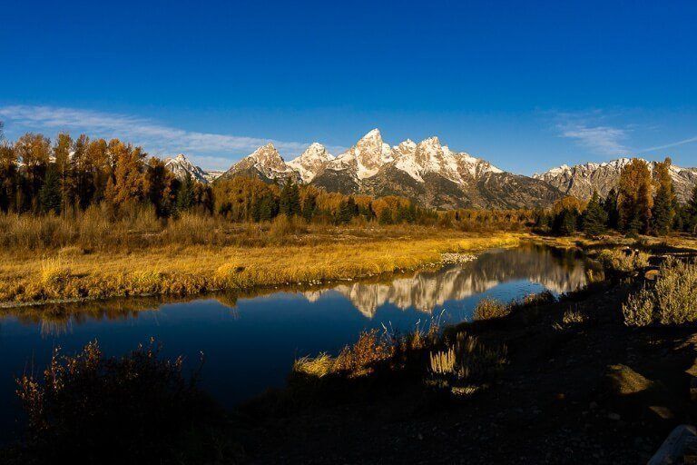 Schwabacher Landing Grand Teton national park at sunrise deep shadows foreground snake river and yellow meadows with mountains background reflecting