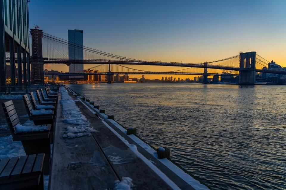 Benches looking out into river from Pier 17 in New York City with orange sky