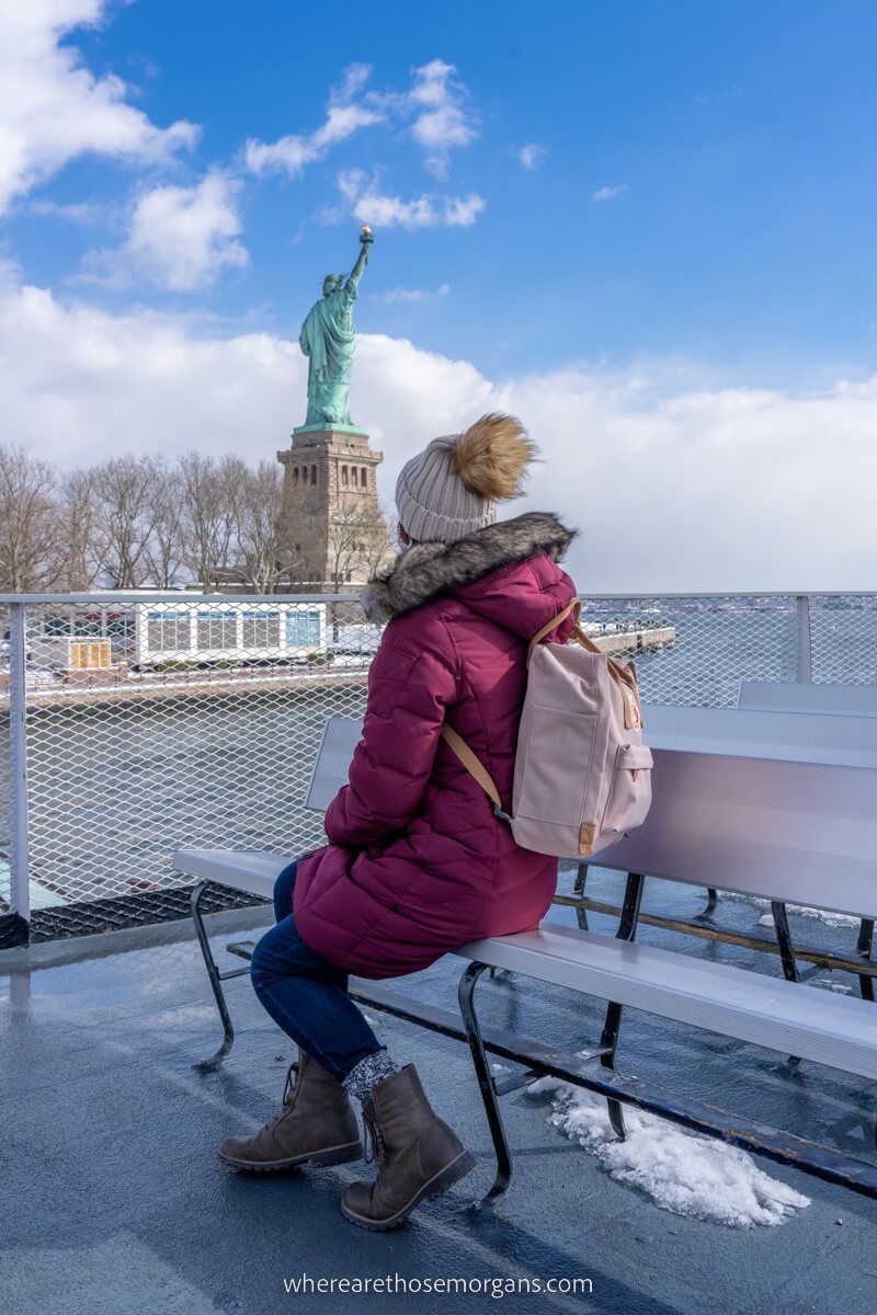 Woman sat on the Statue of Liberty and Ellis Island ferry top deck with coat and hat on a cold day in new york city 