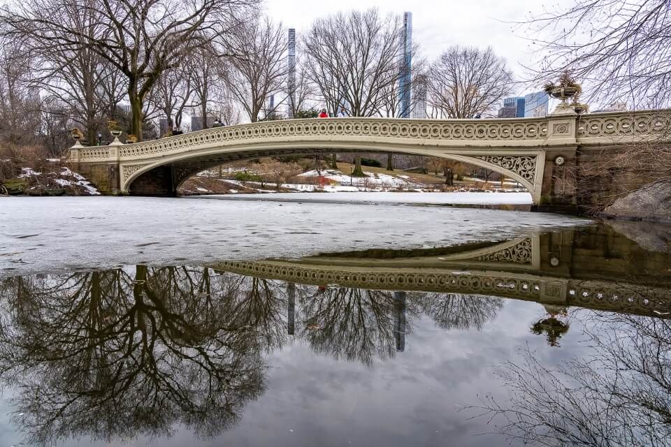 Bow bridge in central park reflecting in water on a snowy day in winter
