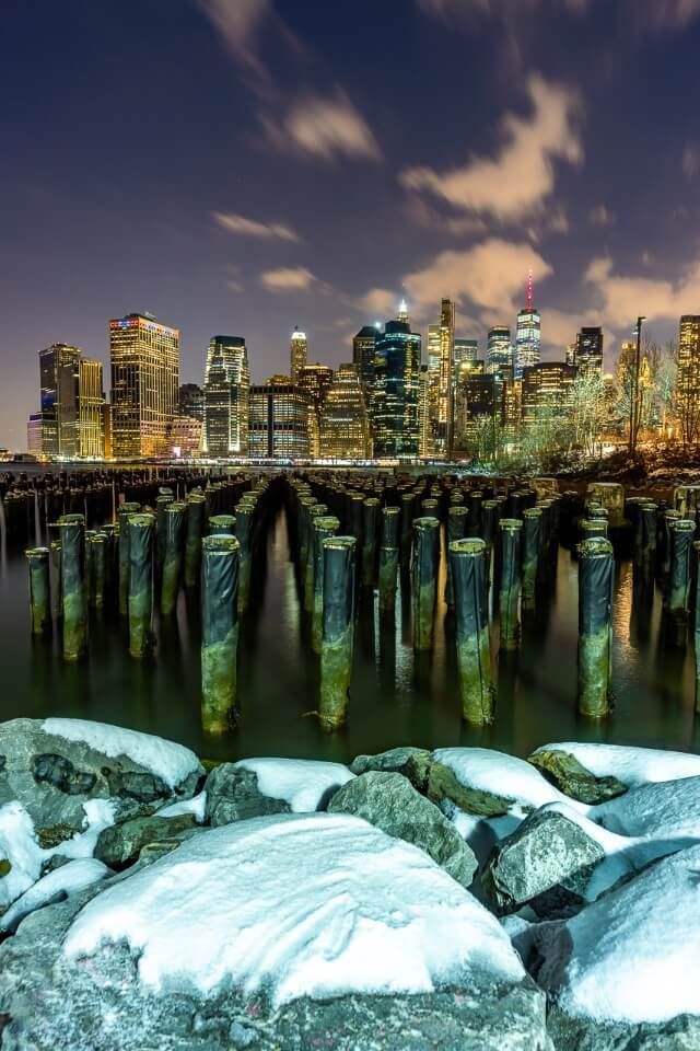 NYC skyline from brooklyn old pier 1 wooden poles and snow on rocks