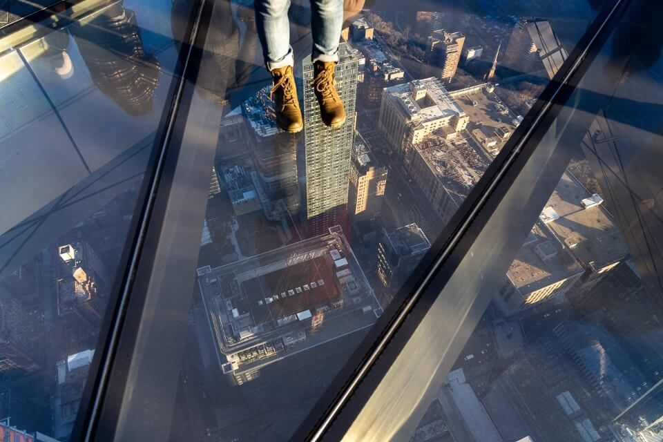 Woman looking down through a glass floor at roads and buildings below Midtown Manhattan 