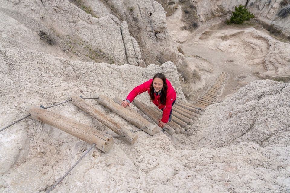 Smiling woman climbing up wooden ladder poles on the notch trail in badlands national park sd