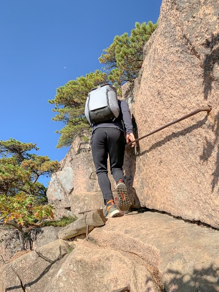 Man climbing along narrow rock edge holding onto iron run bars