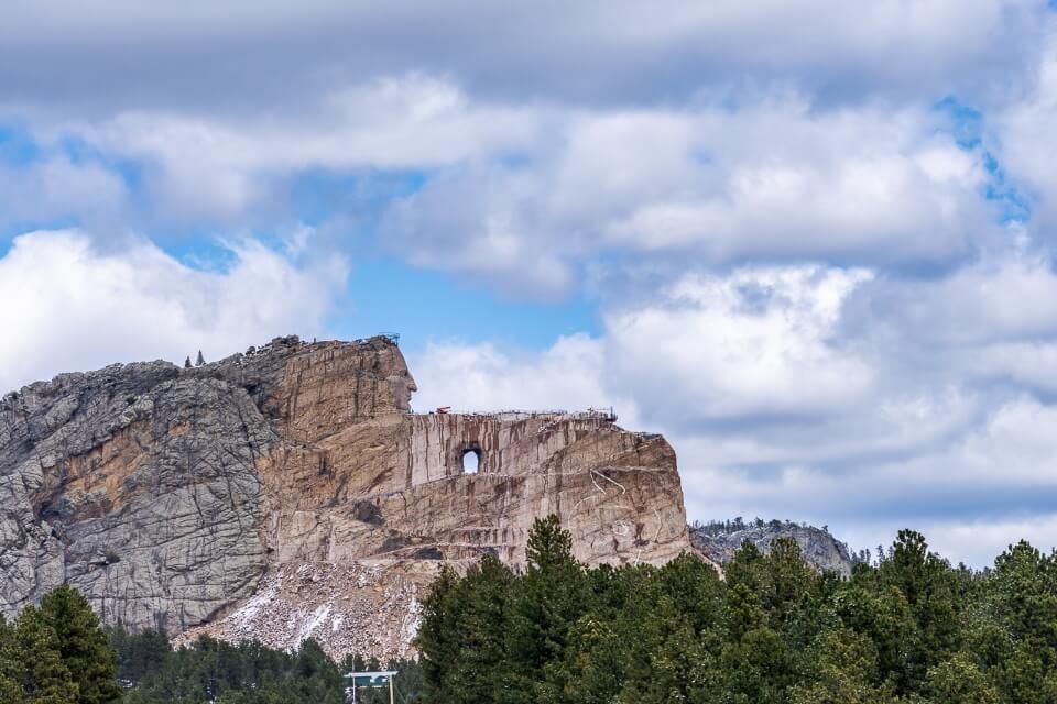 Distant view of Crazy Horse Memorial mountain carving into granite rock on a cloudy day, similar type of attraction to Mount Rushmore but unfinished