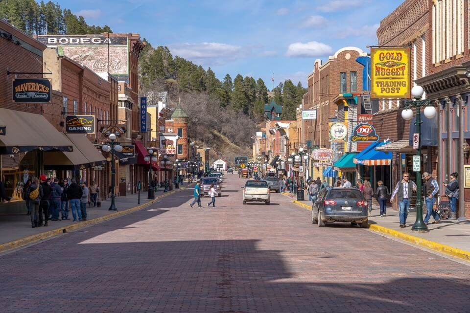 View up the old historic main street in downtown Deadwood SD with wooden building facades and tourists