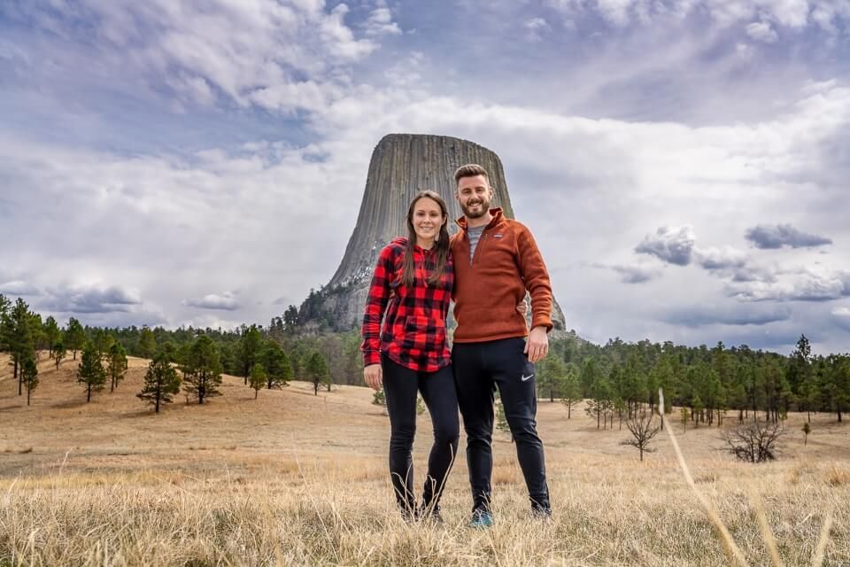 Couple standing together for a photo on wide open field in front of Devils Tower in Wyoming