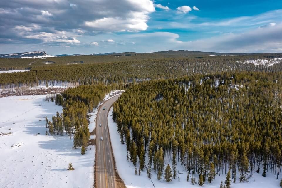 Drone shot of route dissecting a forest covered in snow