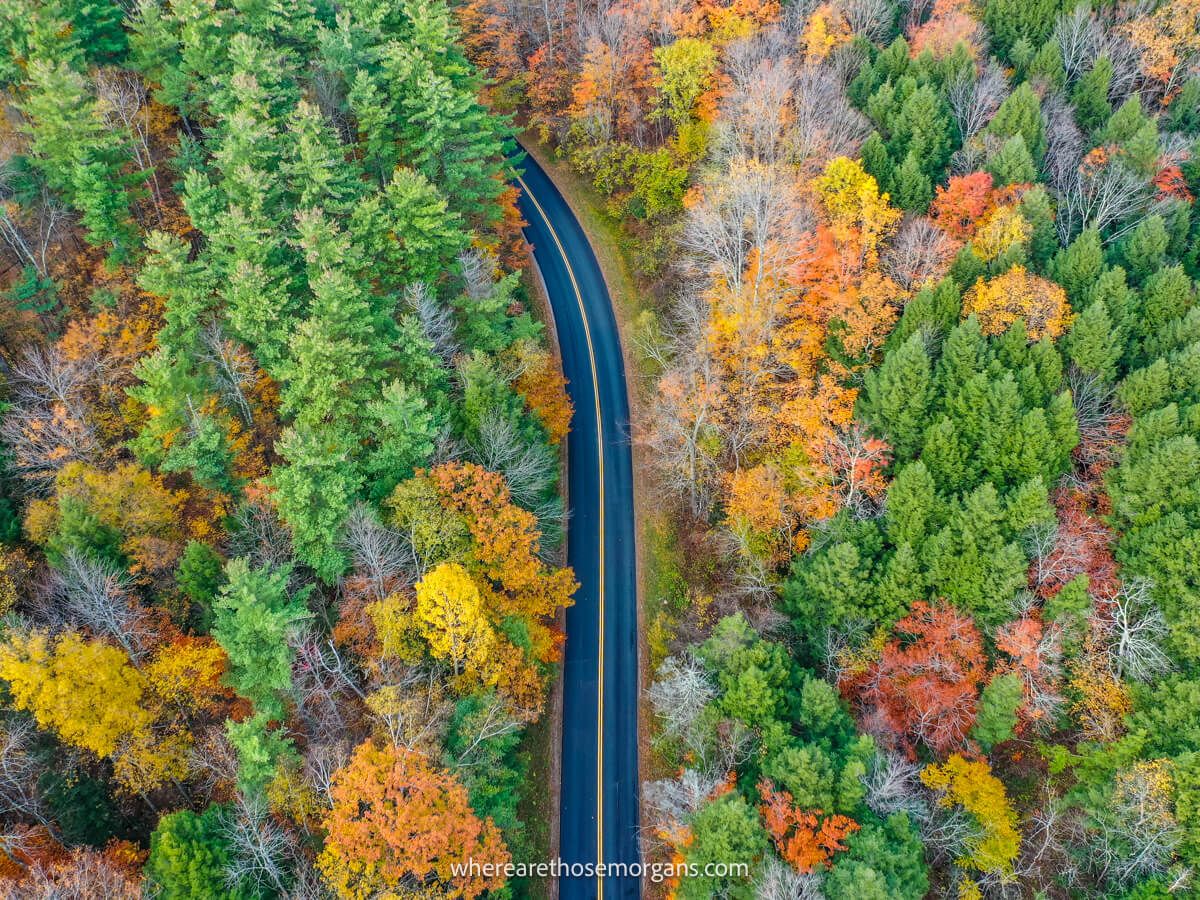 Drone photo from above looking down over a road cutting through a thick forest with colorful leaves on the Kancamagus Highway road trip in New Hampshire during the fall