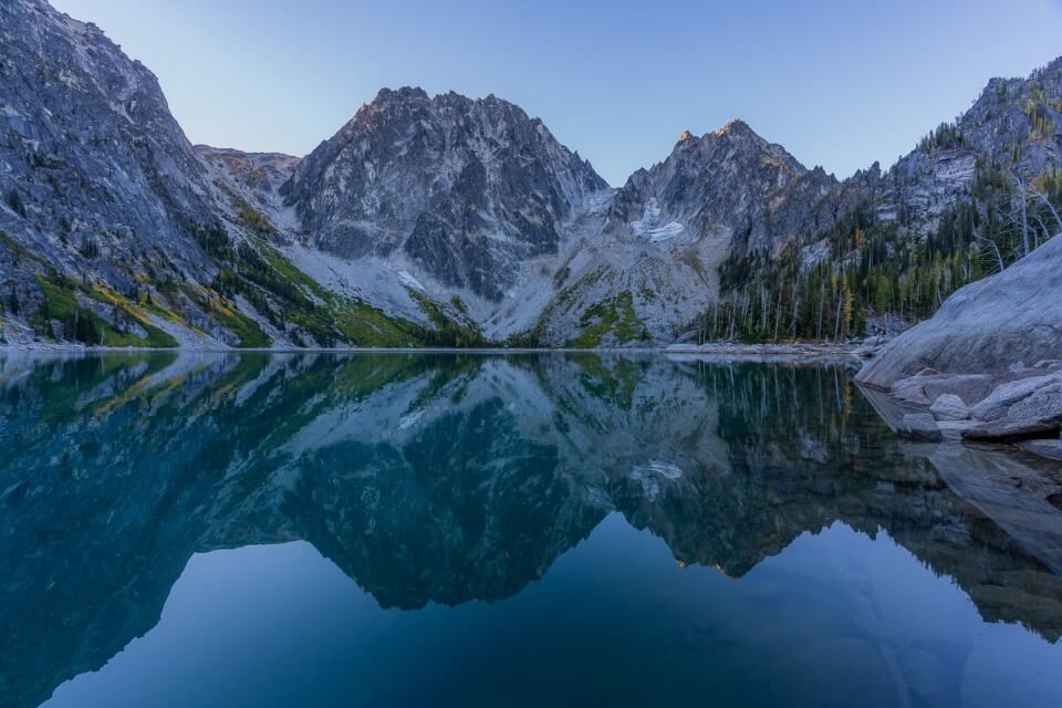 Colchuck Lake at sunrise hiking the amazing enchantments trail in washington mountain peaks reflecting in water Asgard pass to the left