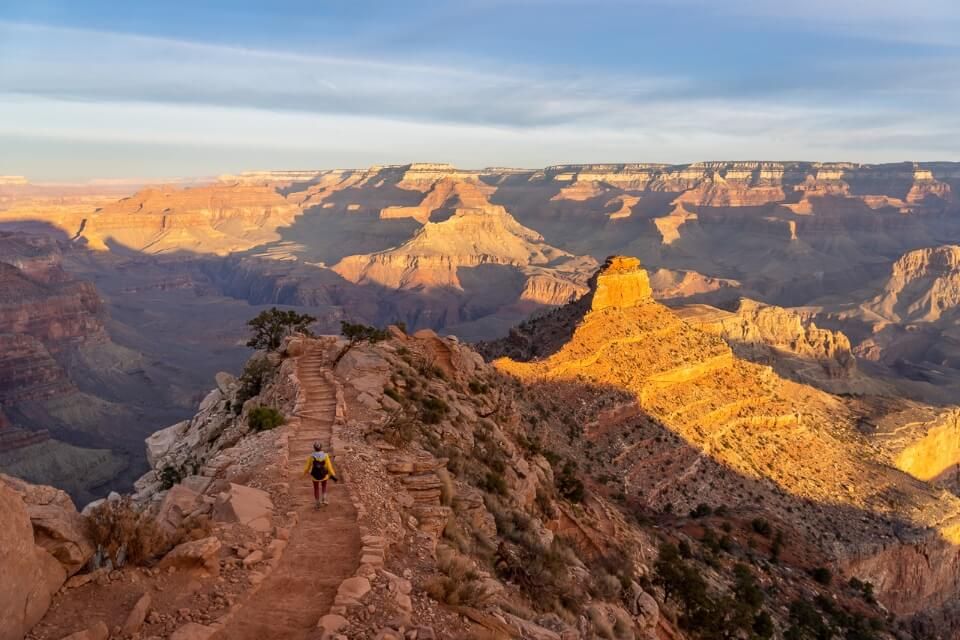 Yaki Point overlooking south kaibab trail at sunrise with hiker enjoying special views of grand canyon south rim