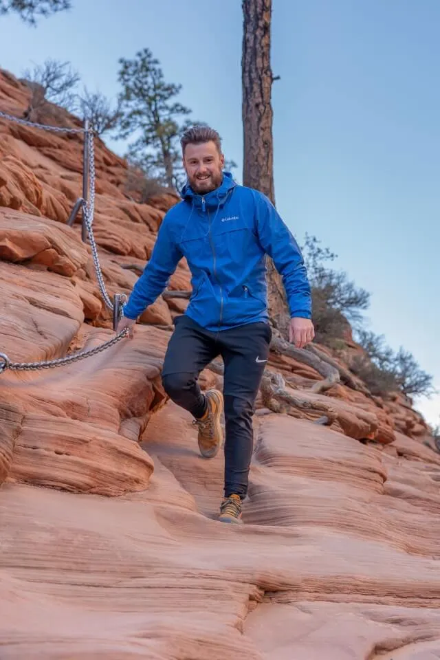 Hiker holding a chain on a steep orange rock face with coat on in Utah