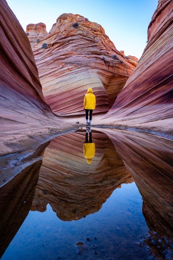 Reflection of hiker in yellow raincoat in shallow still pool in The Wave northern Arizona at sunrise
