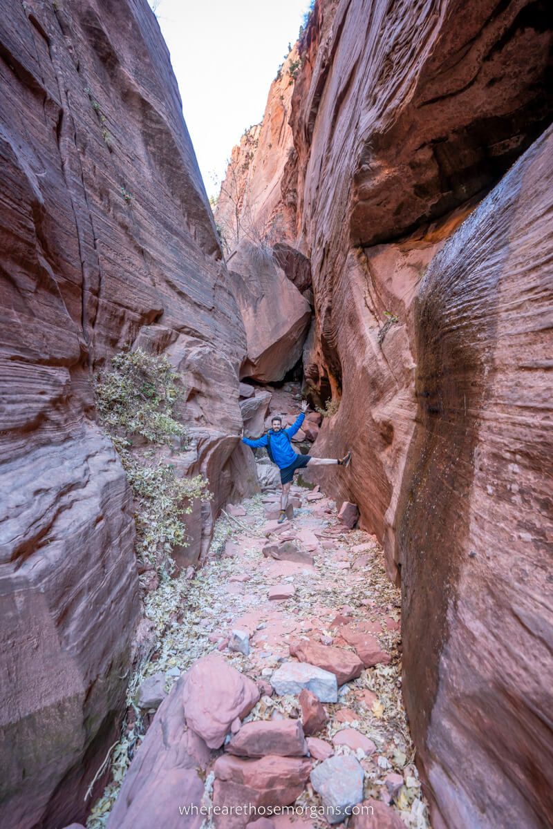 Hiker reaching between tall cliff walls in a v shaped box canyon