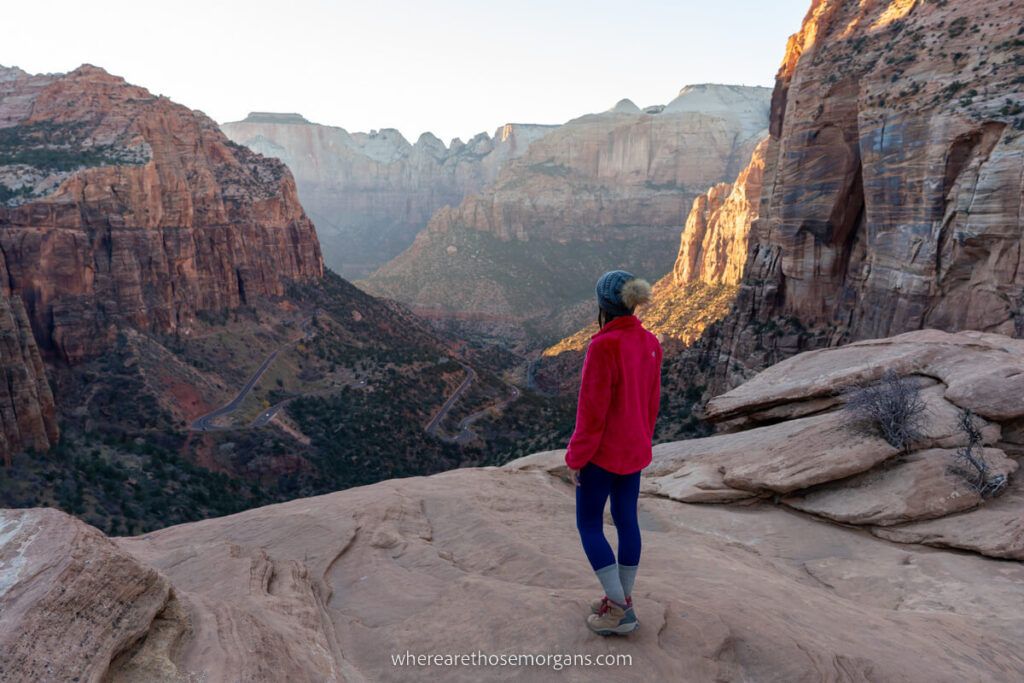 Hiker standing on the edge of a flat rock formation overlooking a deep canyon below at sunset
