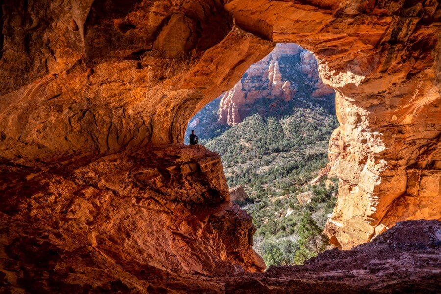 Hiker sat on ledge of Keyhole Cave the largest of the Sedona caves huge chamber with orange light illuminating walls