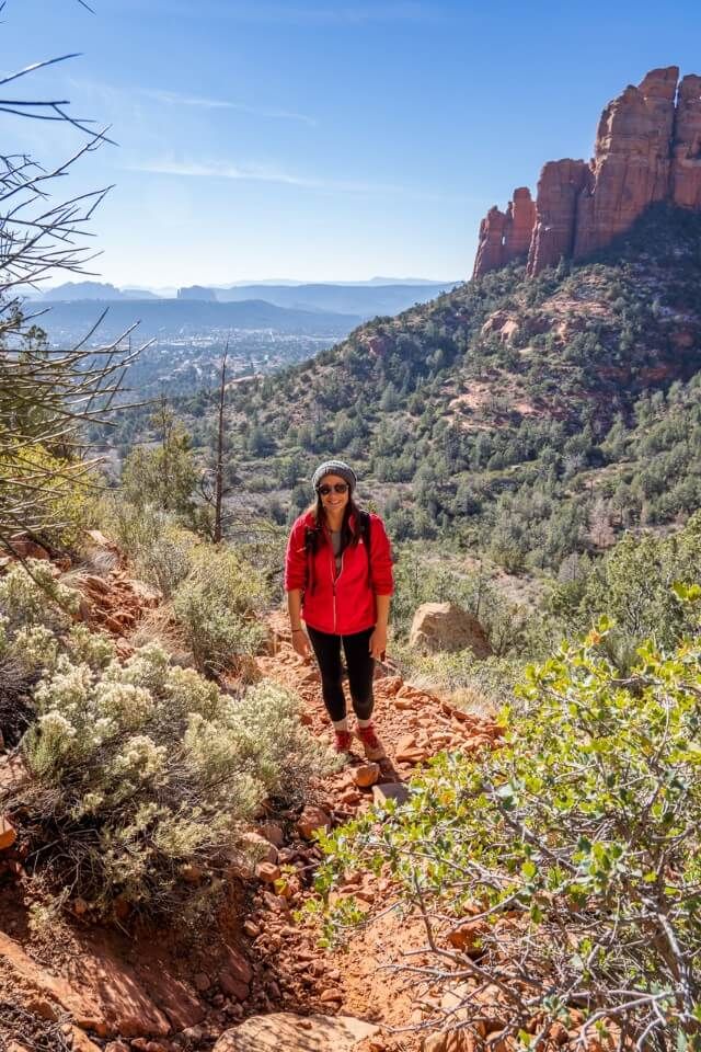 Hiker in red coat on a sunny winter day hiking in red rocks and green vegetation