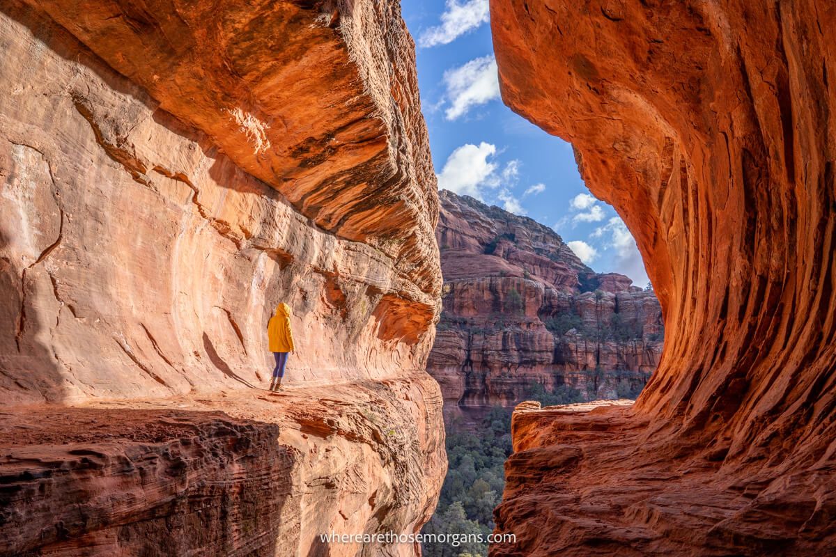 hiker in yellow coat stood inside the sedona subway cave alone on a sunny day