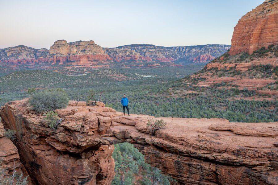 Hiker in blue waterproof coat standing on a natural rock arch formation in arizona