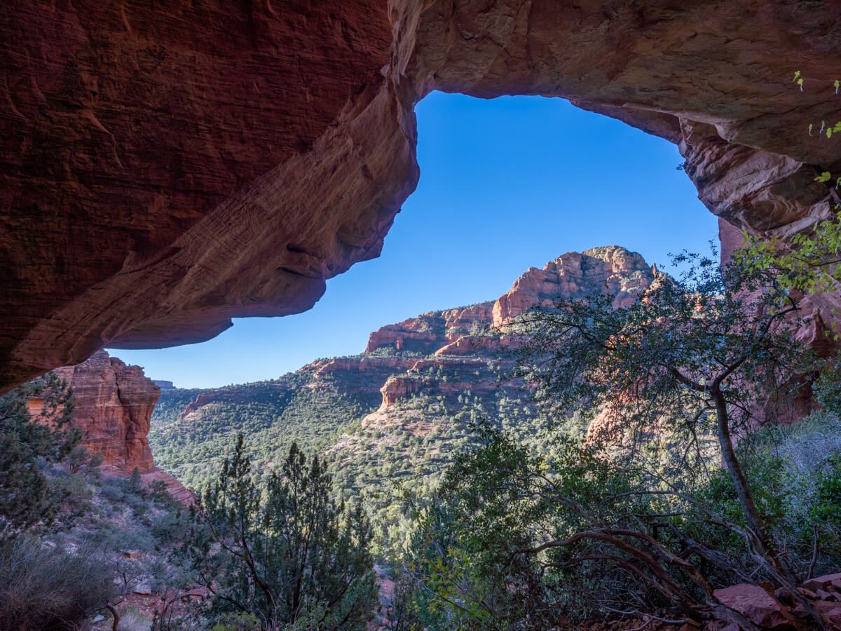 Awesome view through Fay Canyon Arch overlooking Fay Canyon Trail trees and red rocks in Sedona Arizona hike a steep bank to reach the arch