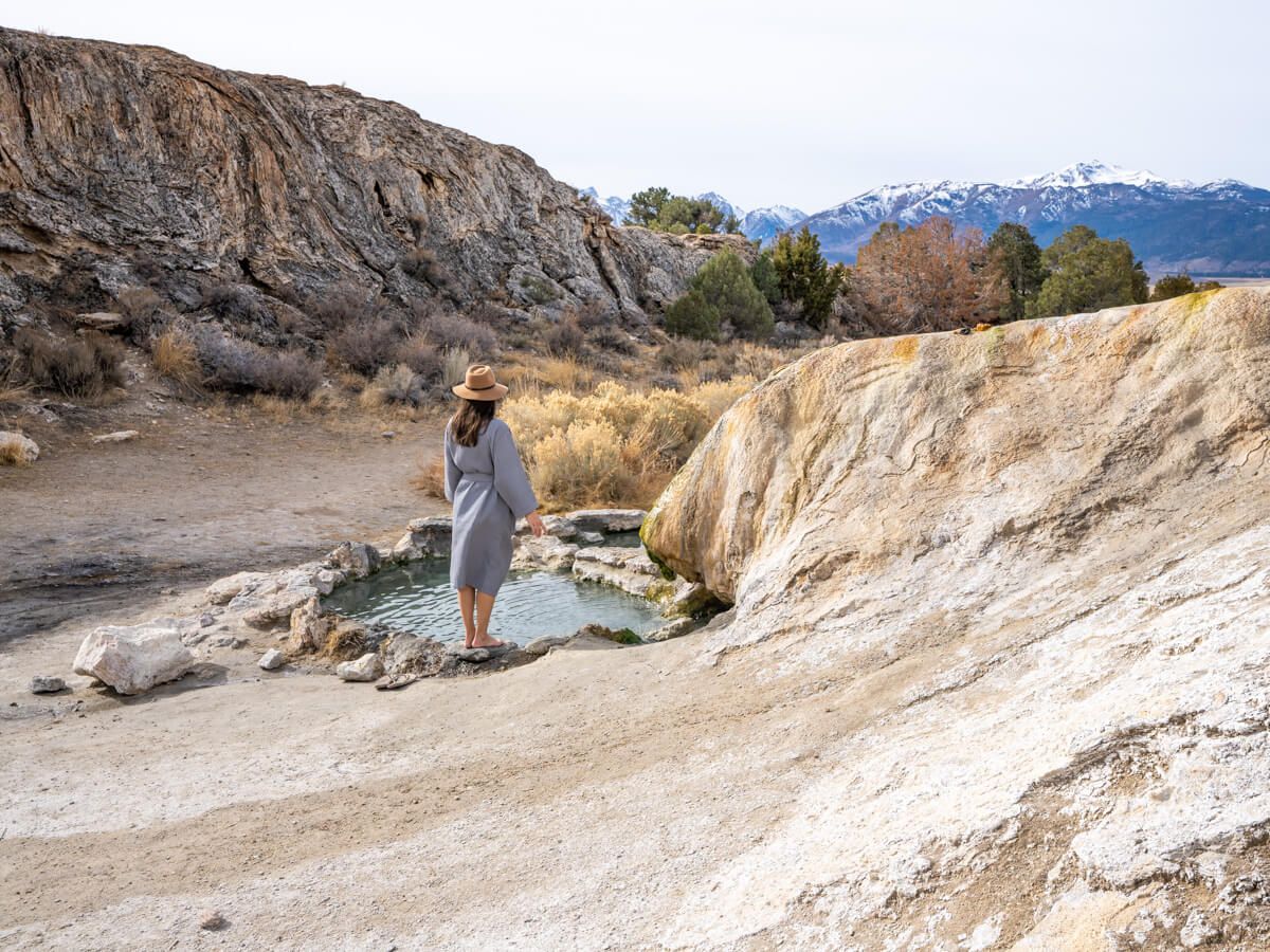 Women standing on the edge of travertine hot springs looking at mountains in the distance