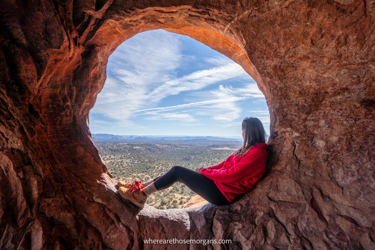 Hiker sat in a small circular opening in a red rock wall