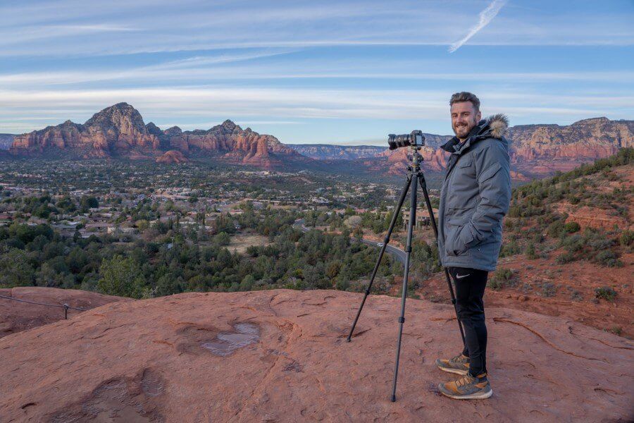 Photographer with camera on tripod at dusk in winter with fur coat in a red rock landscape