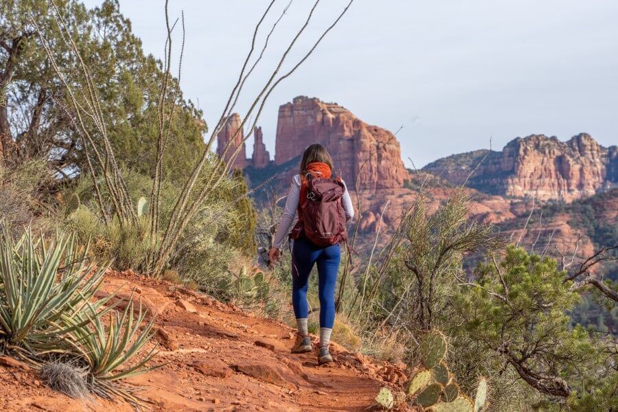 Hiker walking Pyramid Loop Trail with Cathedral Rock in background on a sunny Winter day in Sedona Arizona