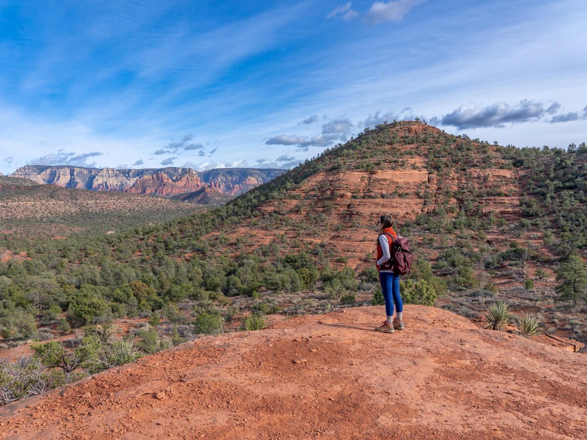 Hiker stood on a small mound looking at expansive views over a red rock landscape in Arizona