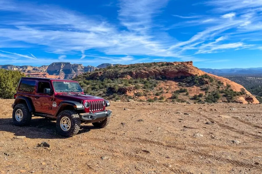 Car parked on a dirt track with blue sky and red rocks behind