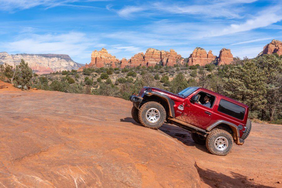 Maroon wrangler climbing a steep rocky gradient with blue sky in northern Arizona